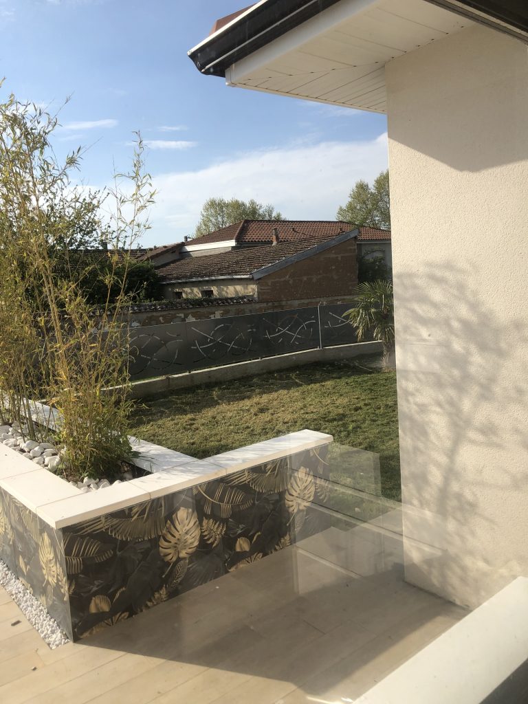 Terrasse carrelée d’une maison, jardinière habillée de carreaux à motif végétal