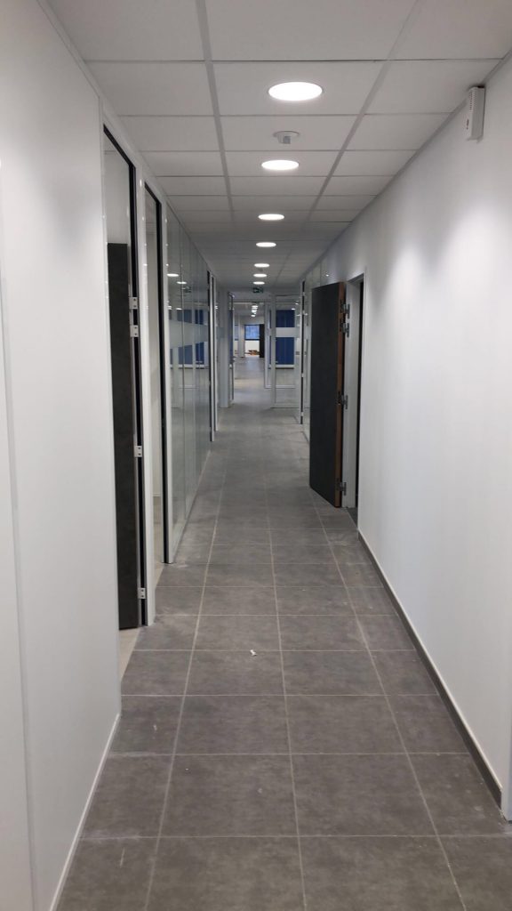 Couloir de bureaux rénové, portes sombres, carrelage gris et éclairage encastré