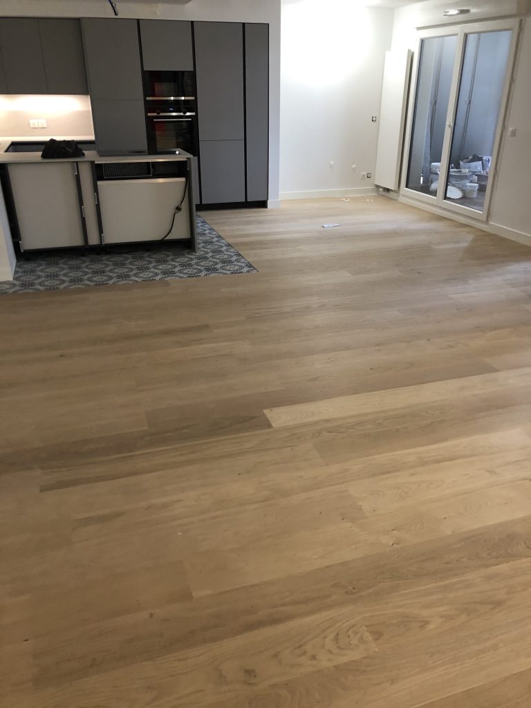 Séjour rénové avec parquet en chêne clair et cuisine ouverte aux façades grises