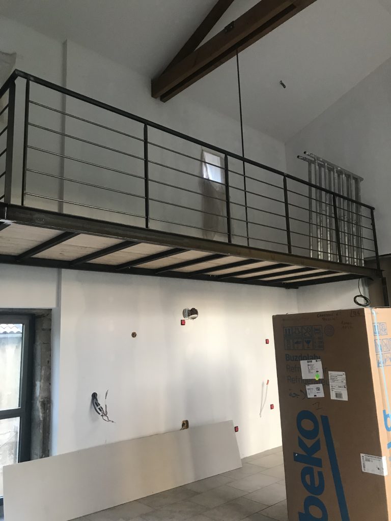 Mezzanine à garde-corps métallique sous une charpente apparente, en cours de travaux