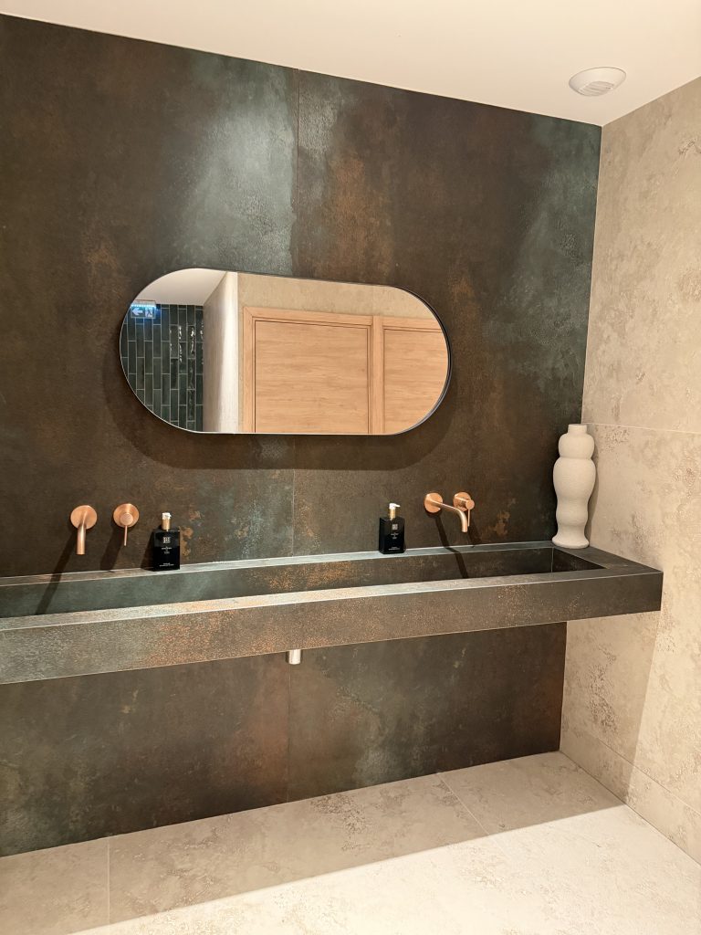 Plan vasque monobloc, mur sombre et miroir ovale dans les sanitaires du D’Calé